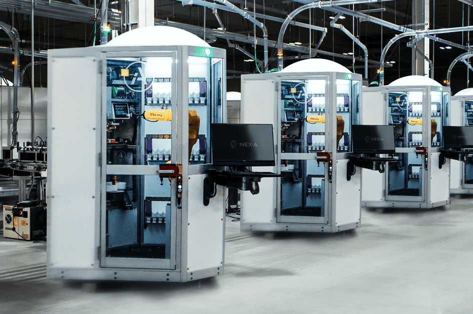 Row of white automated pharmacy machines with glass panels and monitors in a warehouse facility