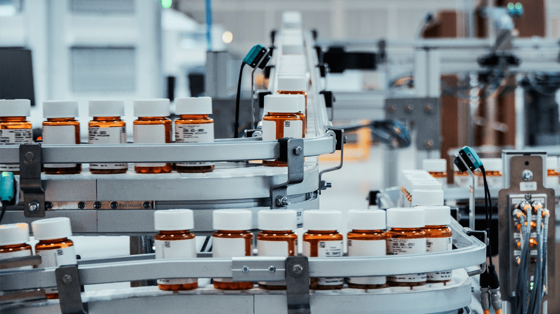 Orange pill bottles on a conveyor belt in a central fill pharmacy