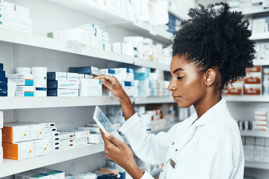 Woman pharmacist looking at tablet and reaching for medicine on the shelf.